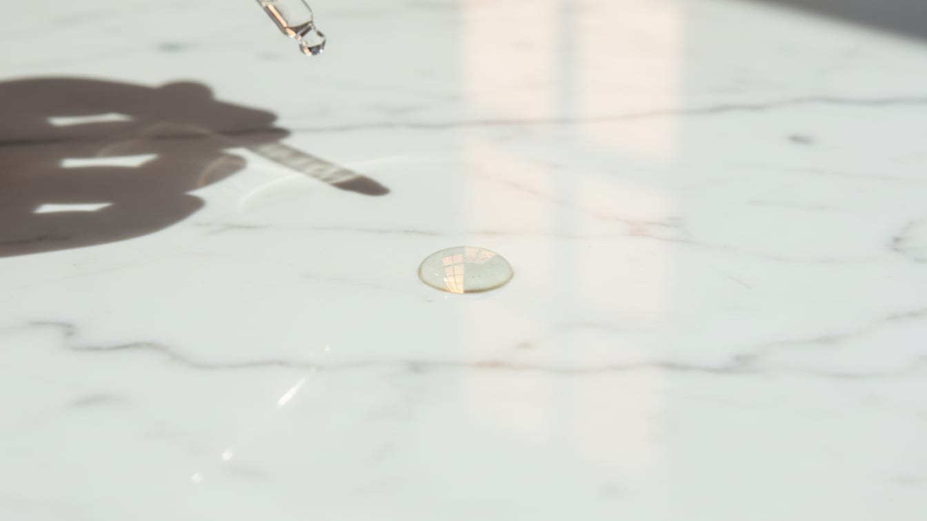 Illustration: A clear serum drop on a cool marble surface, reflecting soft, warm natural light.